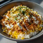 A close-up of the Flavor Street Corn Chicken Rice Bowl, topped with shredded chicken, corn, cotija cheese, and crema.