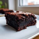 A close-up shot of a single, rich, dark chocolate slice of fudgiest brownies on a white plate.
