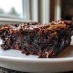 A close-up, side view of a single, incredibly moist and fudgiest brownies square on a white plate.