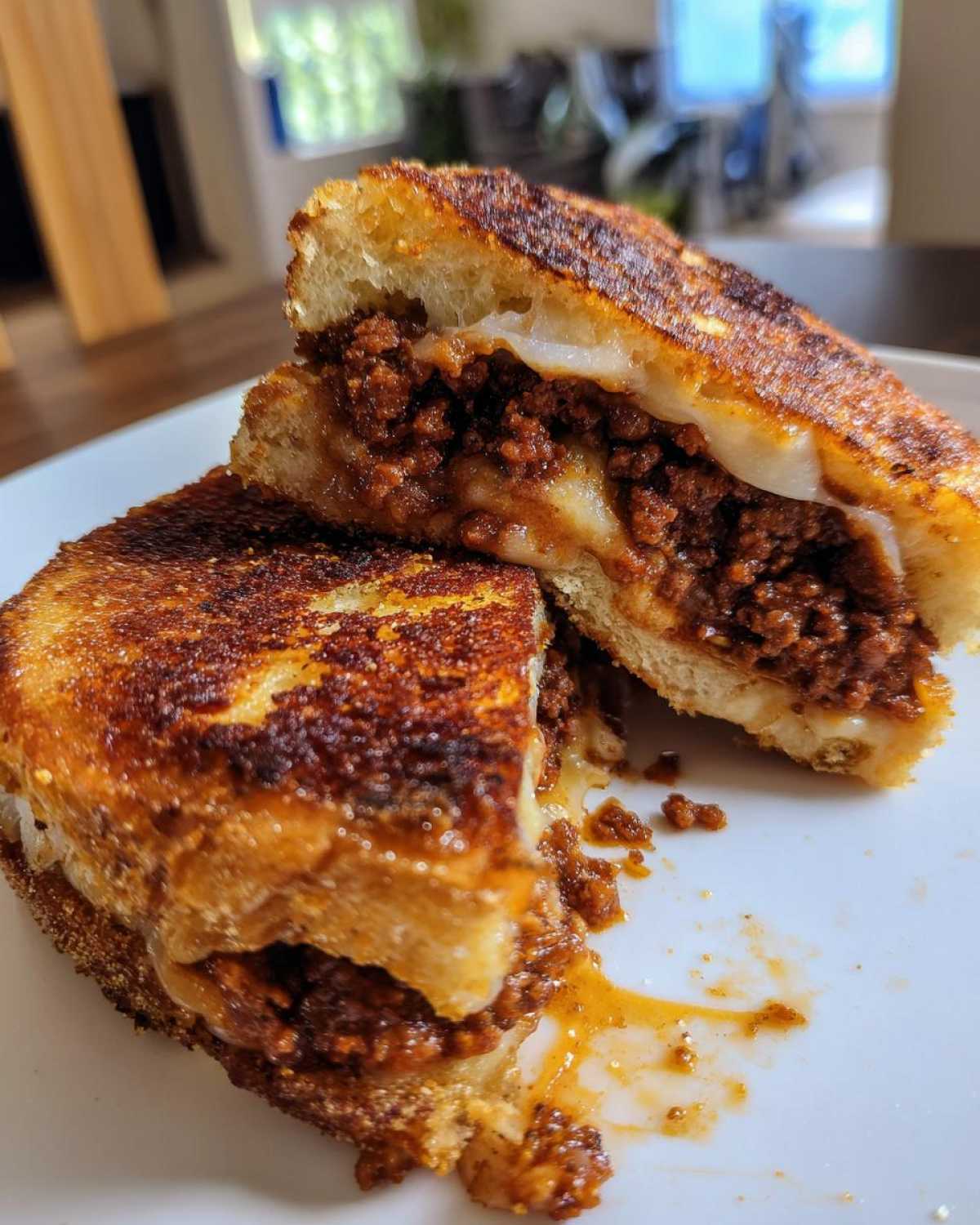 A grilled sandwich, cut in half, revealing a rich, saucy filling and melted cheese, representing Garlic Bread Sloppy Joes.