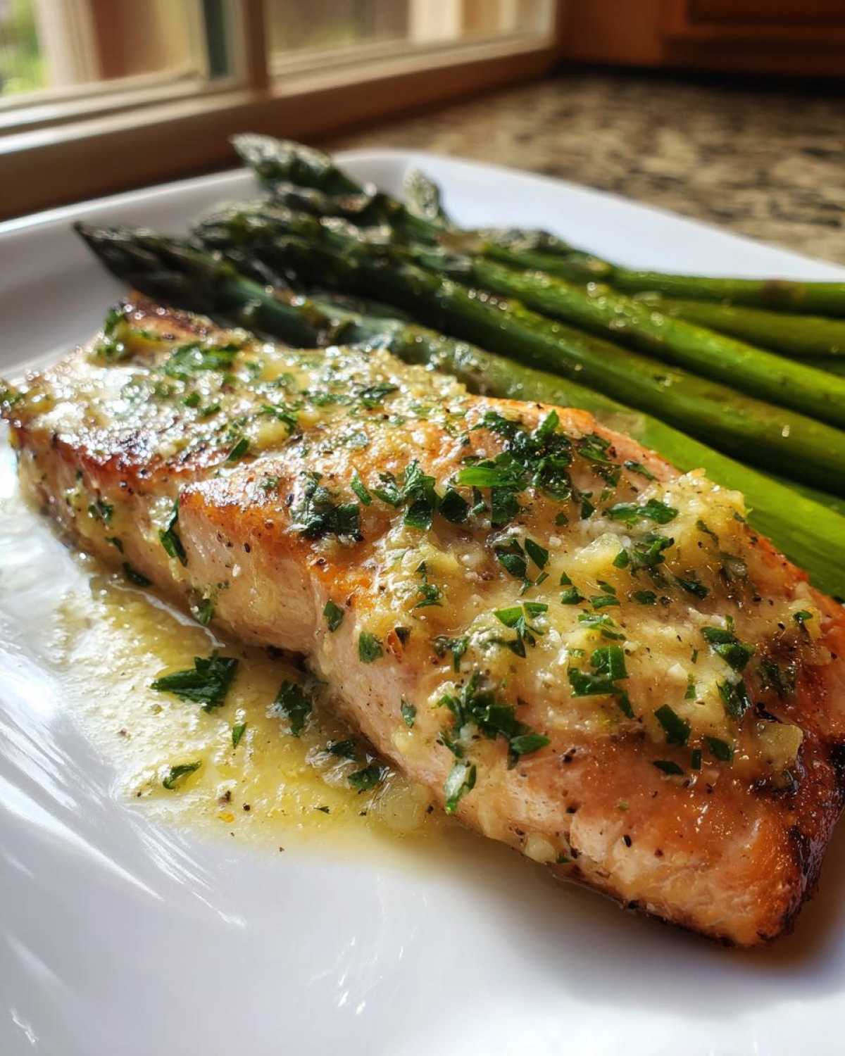 Close-up of a perfectly cooked Garlic Butter Baked Salmon Dinner topped with minced garlic and parsley, served alongside roasted asparagus.