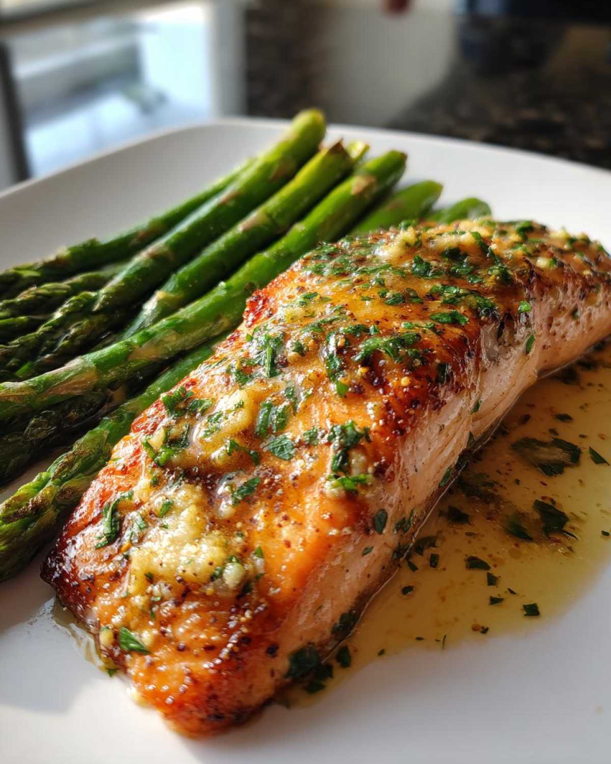 Close-up of a perfectly cooked Garlic Butter Baked Salmon Dinner topped with herbs and served alongside bright green asparagus.