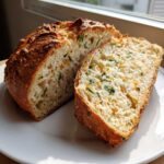 A loaf of Garlic Herb Dutch Oven Bread, sliced open to show the soft interior filled with green herbs and golden crust.