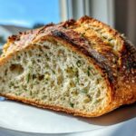 Close-up of a thick slice of Garlic Herb Dutch Oven Bread showing the airy interior studded with green herbs and a dark, crispy crust.