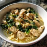 A close-up of Garlic Parmesan Chicken Ramen featuring chunks of chicken and wilted spinach over ramen noodles in a creamy sauce.