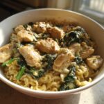 A close-up of Garlic Parmesan Chicken Ramen featuring creamy sauce, chunks of chicken, and wilted spinach over ramen noodles.