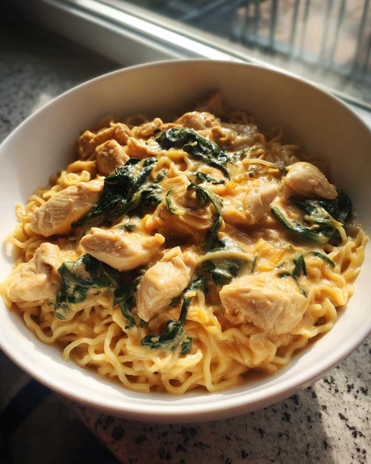 A close-up of creamy Garlic Parmesan Chicken Ramen with chunks of chicken and wilted spinach in a white bowl.