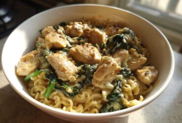 A close-up of Garlic Parmesan Chicken Ramen featuring creamy sauce, chunks of chicken, and wilted spinach over ramen noodles.