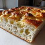 Close-up of a thick slice showing the airy crumb structure of Garlic Parmesan Focaccia Bread with a golden, dimpled top.