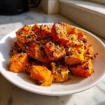 A close-up of crispy Garlic Parmesan Roasted Sweet Potatoes cubes piled on a white plate.
