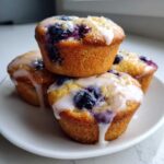 A stack of four golden-brown Lemon Blueberry Muffins topped with a sweet white glaze dripping down the sides.