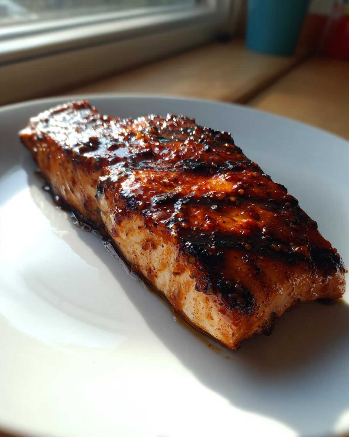 A perfectly cooked, glazed Texas Roadhouse Salmon fillet resting on a white plate, catching bright sunlight.