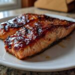 Two perfectly cooked, glazed fillets of Texas Roadhouse Salmon resting on a white plate.