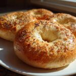 Three golden brown Greek Yogurt Bagels topped with everything seasoning sitting on a white plate.