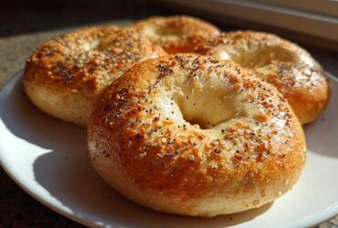 Three golden brown Greek Yogurt Bagels topped with everything seasoning sitting on a white plate.