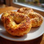 Four golden brown Greek Yogurt Bagels topped with poppy seeds resting on a white plate.