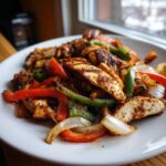 A plate piled high with seasoned, sliced Grilled Chicken Fajitas mixed with sautéed red, green peppers, and onions.