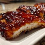 Close-up of a juicy piece of Honey BBQ Chicken, showing the thick, glossy glaze and white interior meat.