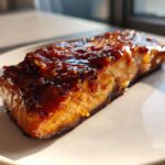 A close-up of a perfectly cooked salmon fillet covered in a thick, shiny Honey Garlic Glazed Salmon sauce with sesame seeds.