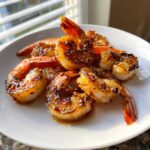 Close-up of perfectly grilled Honey Garlic Grilled Shrimp coated in a shiny glaze and sesame seeds, served on a white plate.