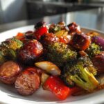 Close-up of glossy, glazed Honey Garlic Kielbasa & Veggies, including roasted broccoli, red peppers, and onions on a white plate.