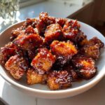 Close-up of crispy Honey Garlic Salmon Bites coated in a thick, glossy, dark sauce and sprinkled with sesame seeds.