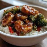 A close-up of a white bowl filled with white rice topped with glossy Honey Garlic Shrimp and bright green broccoli florets.