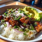 Close-up of a Honey Lime Chicken Avocado Rice Bowl with glazed chicken, white rice, red onion, and sliced avocado.