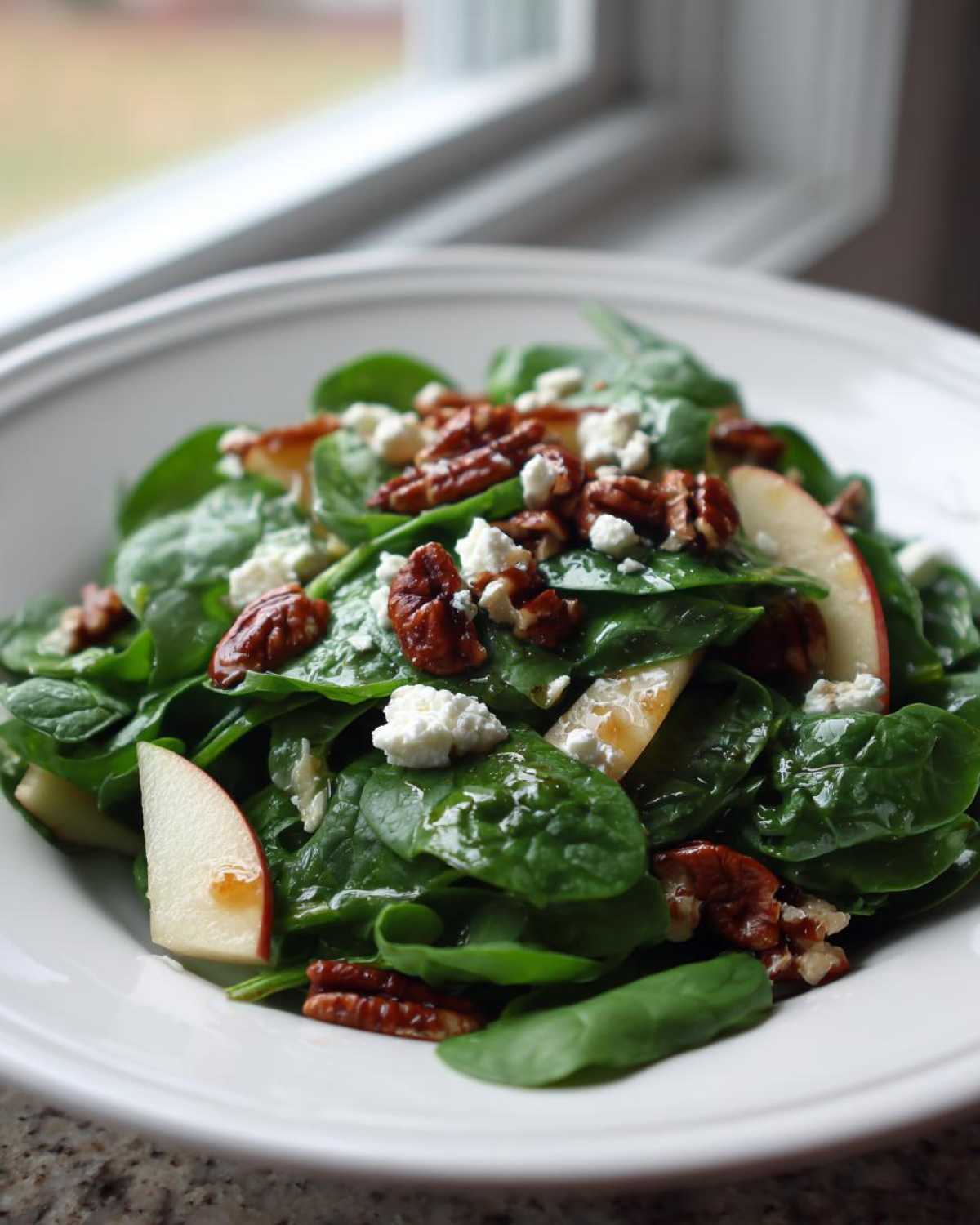 A close-up of a vibrant Honeycrisp Apple Feta Salad featuring spinach, feta crumbles, candied pecans, and apple slices.