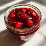 Close-up view looking down into a glass jar filled with chunky Old-Fashioned Strawberry Preserves, showing whole strawberries.