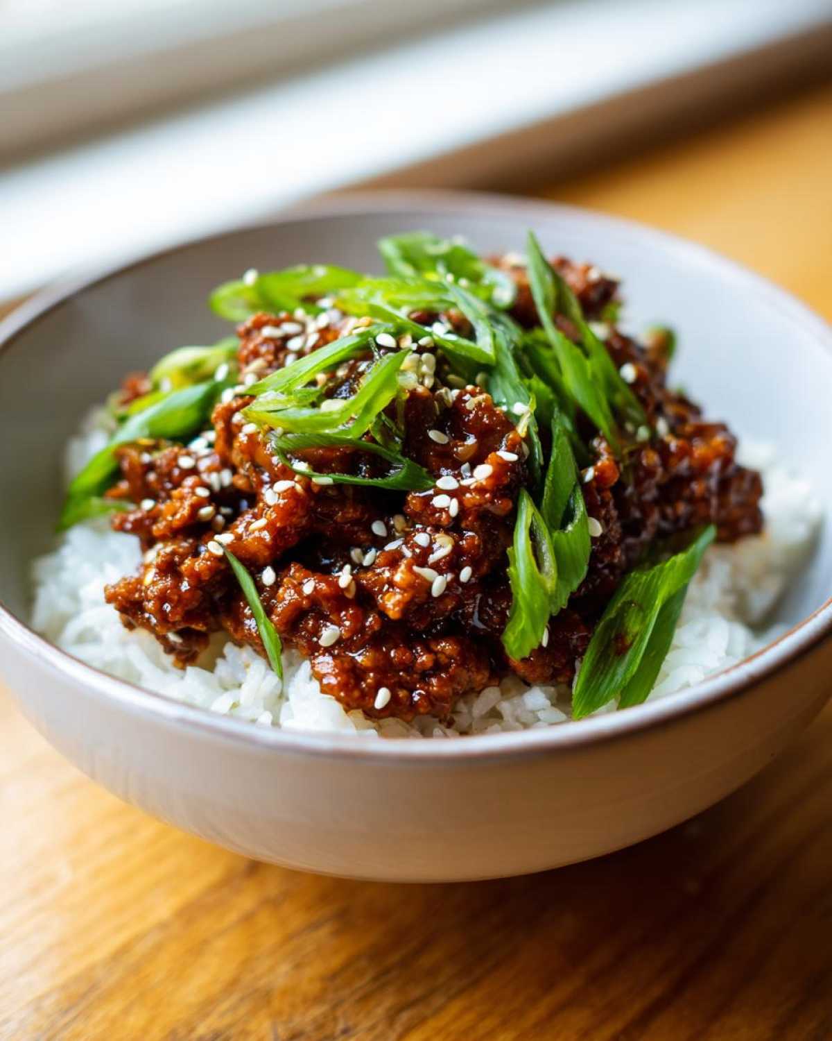 Close-up of a Korean Ground Beef Bowl featuring savory ground beef over white rice, topped with sliced green onions and sesame seeds.