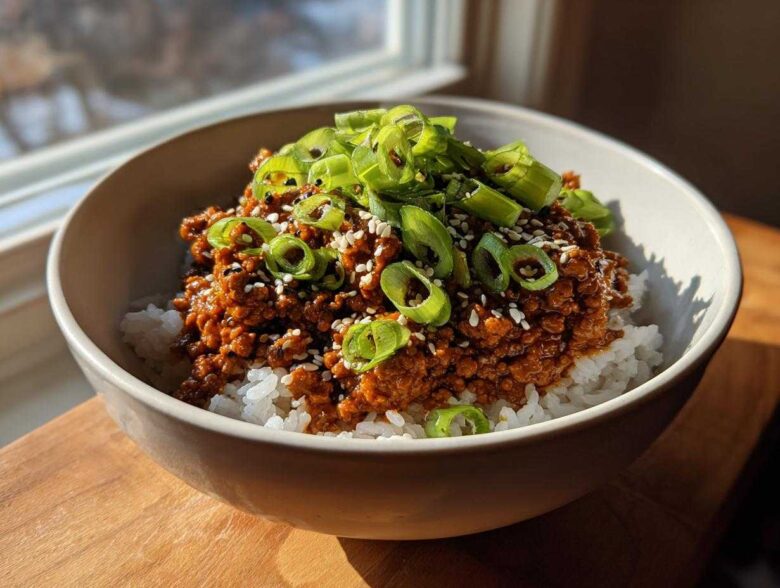 A close-up of a Korean Ground Beef Bowl featuring saucy ground beef served over white rice, topped with sliced green onions and sesame seeds.