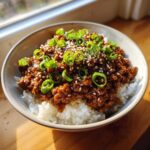 A close-up of a Korean Ground Beef Bowl featuring saucy ground beef served over white rice, topped with sesame seeds and sliced green onions.