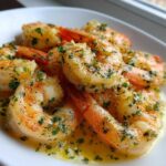 Close-up of juicy Lemon Garlic Shrimp coated in melted butter and fresh chopped parsley served on a white plate.