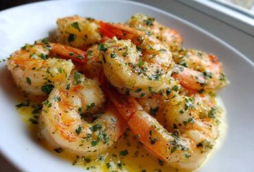 Close-up of juicy Lemon Garlic Shrimp coated in melted butter and fresh chopped parsley served on a white plate.
