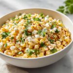 Close-up of a white bowl filled with creamy Mexican Street Corn Salad Esquites, topped with cotija cheese and fresh cilantro.