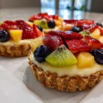 Three vibrant Mini Fruit Tarts featuring strawberries, blueberries, kiwi, and pineapple on a creamy custard filling.