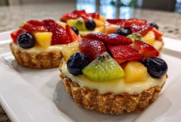 Three vibrant Mini Fruit Tarts featuring strawberries, blueberries, kiwi, and pineapple on a creamy custard filling.