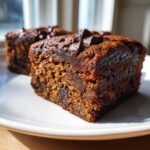 Close-up of two rich, dark Banana Bread Brownies topped with melted chocolate chips on a white plate.