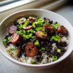 A white bowl filled with One-Pot Black Beans and Rice with Sausage, topped with seared sausage slices and green onions.