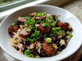 A white bowl filled with One-Pot Black Beans and Rice with Sausage, topped with sliced smoked sausage and green onions.
