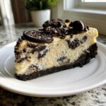 A perfect slice of Oreo Cookies and Cream Cheesecake on a white plate, topped with crushed cookies.