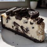 A generous slice of Oreo Cookies and Cream Cheesecake with a dark crust and cookie pieces throughout.