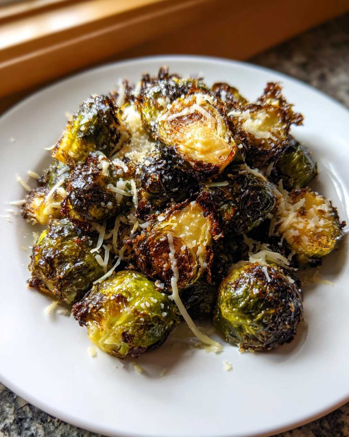 Crispy, caramelized Oven Roasted Brussels Sprouts with Parmesan cheese sprinkled on top, served on a white plate.
