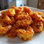 A close-up of crispy Panko Oven Baked Bang Bang Shrimp coated in a glistening, spicy orange sauce, served on a white plate.