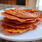 A stack of crispy, baked Pepperoni Cheese Crisps Low Carb Snack piled on a white plate.