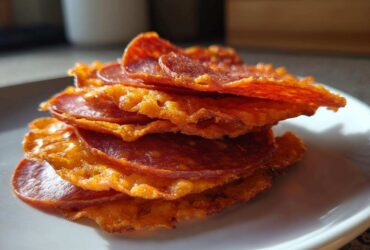 A stack of crispy Pepperoni Cheese Crisps Low Carb Snack, showing melted cheese fused with pepperoni slices on a white plate.