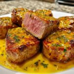 Close-up of seared Pork Medallions served on a white plate, coated in a vibrant yellow sauce with herbs.