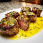 Five perfectly seared Pork Medallions resting in a bright yellow, herb-flecked sauce on a white plate.