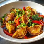 Close-up of golden brown potstickers mixed in a vibrant Potsticker Stir Fry with red peppers and broccoli, topped with green onions.